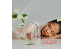 A female model rests her head on a laboratory table decorated with flowers and other beautiful botanicals.